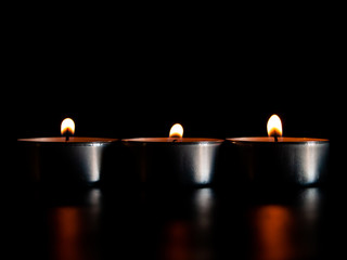 Three lighted candles with an orange flame and isolated on a black background