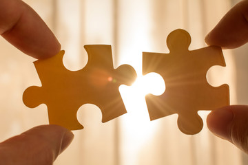 two hands trying to connect couple puzzle piece. with sunset background. symbol of association and connection, business strategy, completing, team support and help concept - obrazy, fototapety, plakaty