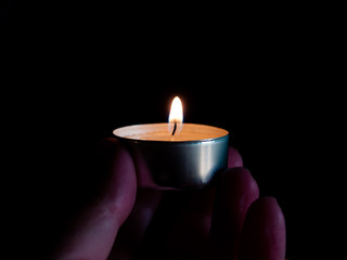 One person with a lighted candle with an orange flame in their hand and isolated on a black background
