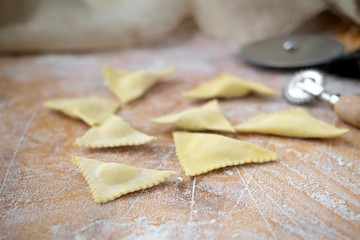 raw triangular ravioli on a wooden kitchen table in flour, cooking homemade pasta