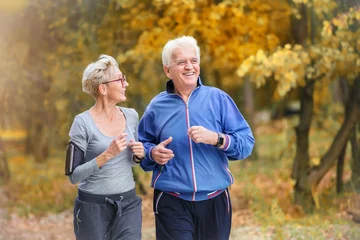 Foto op Plexiglas Smiling senior active couple jogging together in the park © lordn