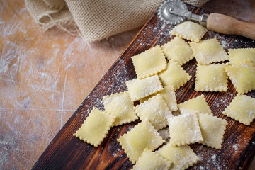 Preparing fresh homemade ravioli at the kitchen wooden table with flour. Top view