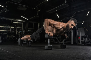 Fototapeta na wymiar Young handsome male athlete bodybuilder weightlifter with idial abdominals, doing exercises in modern gym on a dark background. Exercises for biceps. 