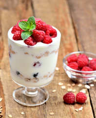 Yogurt with oatmeal and fresh raspberries in a glass and mint leaves - vertical photo