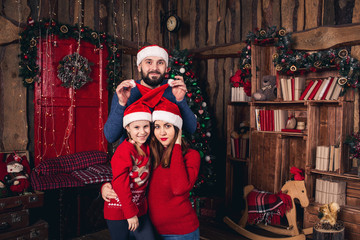 Happy family in Christmas hats sitting in a room in a rustic style. Father raises hats to his wife and daughter.