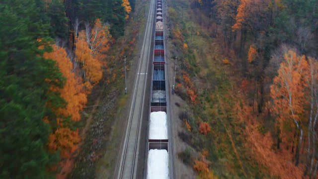 Aerial following shot of a freight train moves through the autumn forest