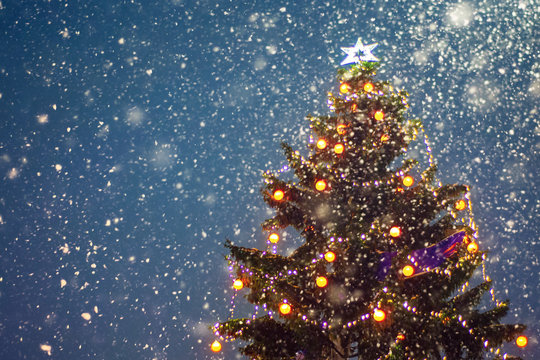 Illuminated christmas tree at night with falling snow and copy space