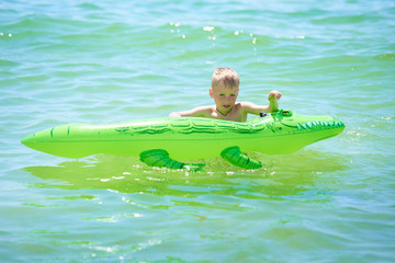 boy swims in the sea on a toy inflatable crocodile