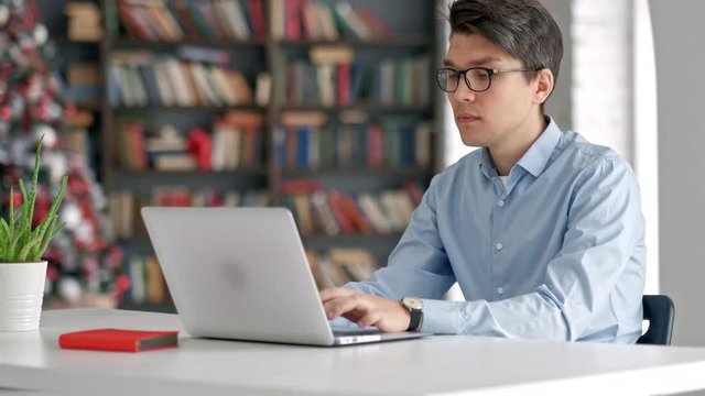 Male university student looking at laptop screen thoughtfully while doing homework. Closeup of concentrated boy trying to fulfill difficult task while studying
