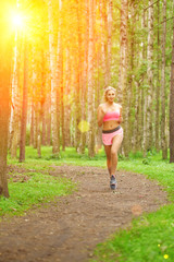 Young woman sports, running in the park. Girl model runs at sunrise or sunset outdoors. Healthy lifestyle, jogging.