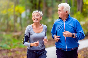 Poster Smiling senior active couple jogging together in the park © lordn