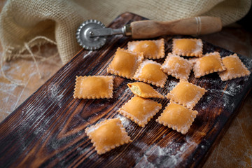 Uncooked rustic style ravioli orange color on a kitchen wooden table