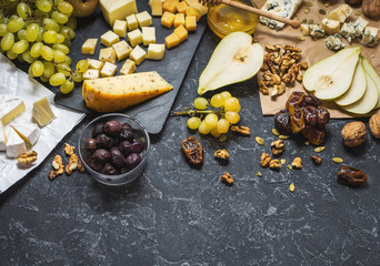 Different types of cheese on board, olive, fruits, almond and wine glasses on black stone table