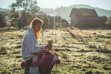 girl sits on a wooden bench in the mountains in nature, reads a book, drinks hot tea from a thermo...