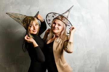 Portrait of two happy young women in black witch halloween costumes on party over background. concept of Halloween . funny faces