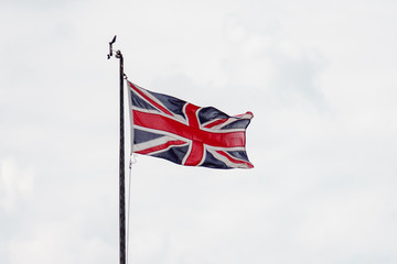 flagpole with flag of great britain flapping in the wind on background of thick white clouds