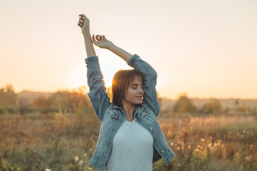 Autumn Girl enjoying nature on the field. Beauty Girl Outdoors raising hands in sunlight rays. Beautiful Teenage Model girl