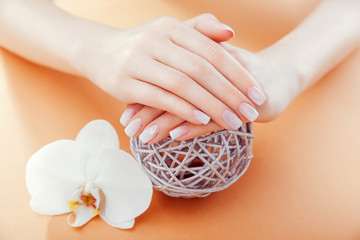 Ombre french manicure with orchid on orange background. Woman with white ombre french manicure holds orchid flower © maryviolet