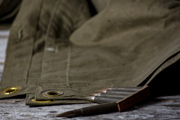 Holder with cartridges 7,92 x 57 - rustic ammos and poncho lies on the wooden background