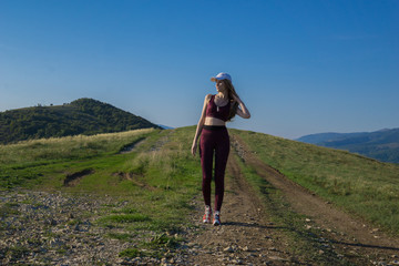 Young athletic girl walks in the mountains against the blue sky