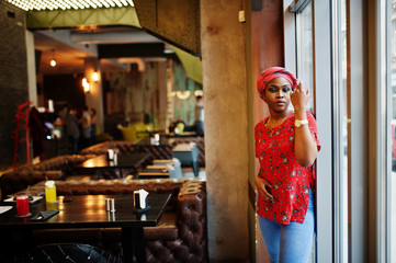 Stylish african woman in red shirt and hat posed indoor cafe.