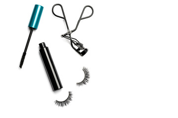 An open bottle of mascara with a black body and blue-green cap, black steel eyelash curler, and 2 long dramatic false eyelashes arranged on the left side on white background shot with studio light