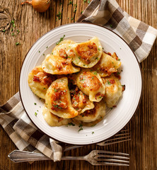 Fried dumplings stuffed with cabbage and meat sprinkled with bacon greaves and chopped parsley on a white plate on a wooden rustic table, top view.
