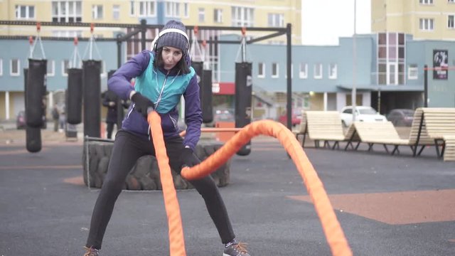 Woman athlete engaged in crossfit with ropes on the street playground,slow mo