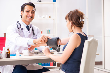 Fototapeta premium Young doctor checking woman's blood pressure