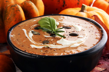 Roasted pumpkin and carrot soup with cream and pumpkin seeds on wooden background.