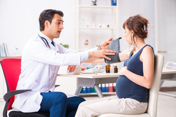 Young doctor checking pregnant woman's blood pressure