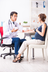 Fototapeta premium Young doctor checking pregnant woman's blood pressure