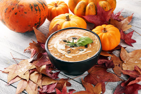 Roasted pumpkin and carrot soup with cream and pumpkin seeds on wooden background.