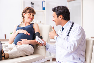 Fototapeta premium Young doctor checking pregnant woman's blood pressure
