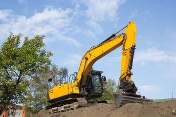 yellow excavator on the soil pile against blue sky
