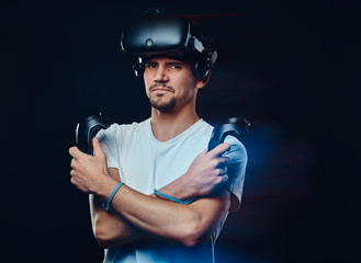 Serious pro gamer wearing virtual reality glasses and holds joysticks, posing with crossed arms.