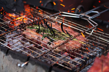 Grilling steaks on flaming fire with rosemary