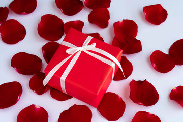 Red gift box with rose petals on white background.