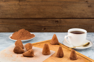 Homemade chocolate truffles on baking paper, cocoa powder, tea in white mug, wooden background.