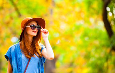 Redhead girl in sunglasses and hat in the autumn park.