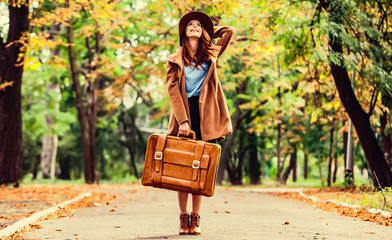 Redhead girl with suitcase in the autumn park.