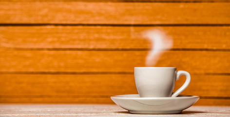 White cup of coffee or tea with steam on wooden background