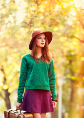 Beautiful redhead girlin green sweater with suitcase in the park.