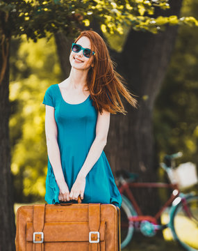 Redhead girl with suitcase in the park. Summertime season