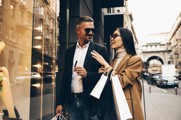 Shopping. Black Friday. Couple. Love. Man and woman with shopping bags and credit card are talking and smiling while walking down the street - obrazy, fototapety, plakaty