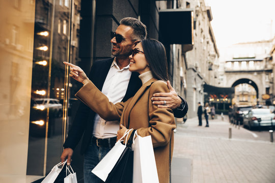 Shopping. Black Friday. Couple. Love. Man And Woman With Bags Are Looking At The Shopping Windows And Smiling While Walking Down The Street