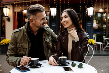 Autumn walk. Cafe. Couple. Love. Man and woman in warm casual clothes are drinking coffee, talking and smiling while sitting in the cafe outdoors