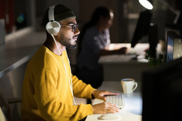Side view portrait of contemporary Middle-Eastern man working late at night using computer  in dark office