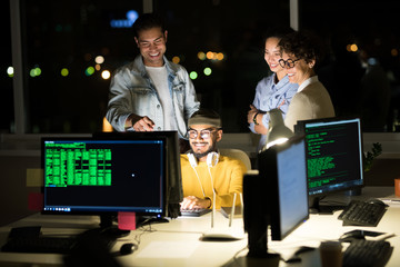 Group of excited young people standing over computer while finishing startup project at night