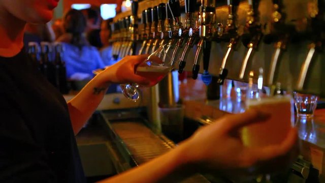 Young woman is pouring two draft beers - Filmed in a small microbrewery pub during a concert